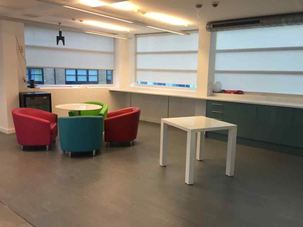 Office breakout area with multi-coloured tub chairs and green gloss kitchen