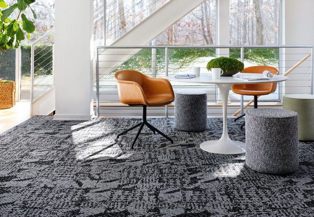 Shaw Contract Houndstooth carpet tiles in grey and black colours fitted in office meeting room with white circular meeting table, poufs and brown leather low back swivel chairs