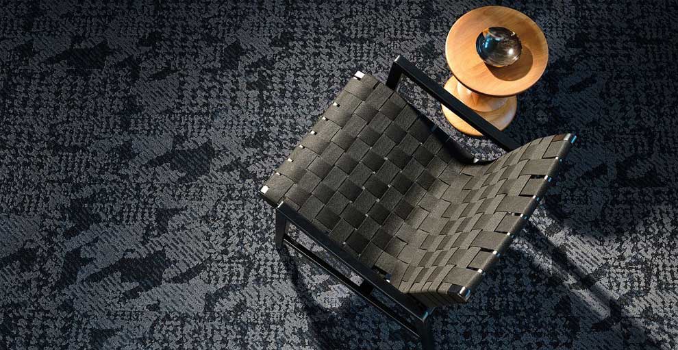 Close up Houndstooth carpet Tile in Mohair colourway shown from above and incorporating a black chair and natural wood circular coffee table on central column